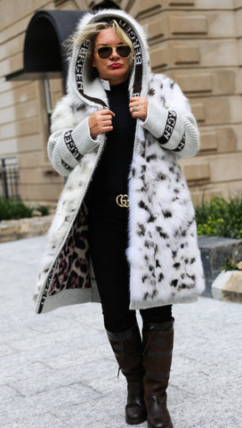Women wearing a luxury white fur coat with black and white pattern, black dress, and brown boots in an urban setting.